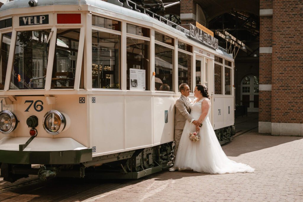 Bruidspaar kijkt elkaar liefdevol aan voor vintage tram tijdens bruiloft in Barneveld, Gelderland