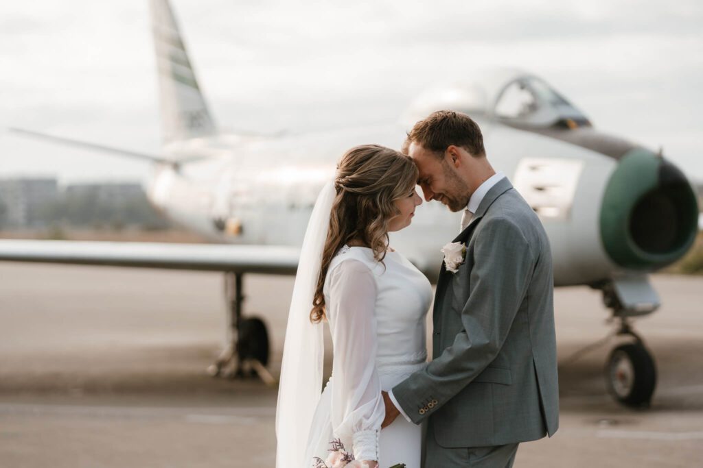 Bruidspaar kijkt elkaar innig aan voor vliegtuig op vliegbasis van Soesterberg, Utrecht